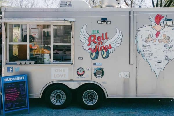 DKL Roll -n- Wings silver food truck with Bud Light sandwich board listing menu.