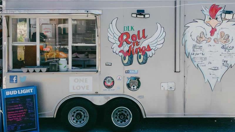 DKL Roll -n- Wings silver food truck with Bud Light sandwich board listing menu.